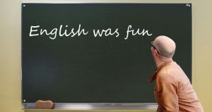 Lehrer vor Tafel, auf der 'English was fun' steht