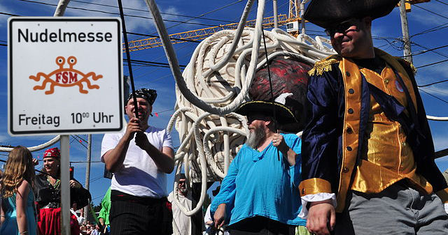 Pastafari mit Piratenkostümen und Hinweistafel auf Nudelmesse am Freitag